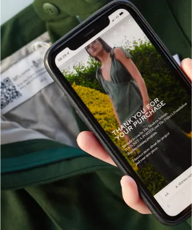 A smartphone scanning a Digital ID in the form of a QR code stitched into a pair of Modern Artisan trousers by YOOX Net-a-Porter